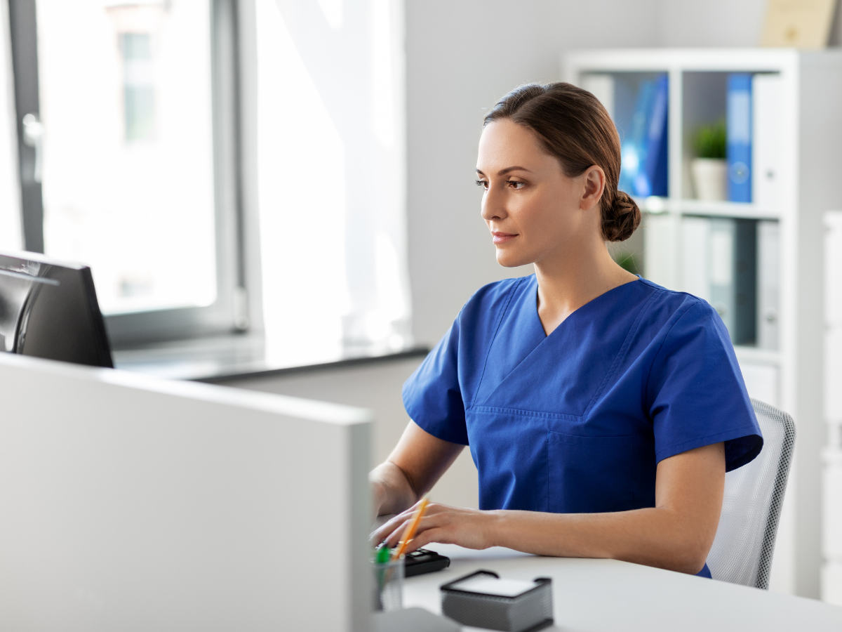 Eye care staff member working at a computer to manage compliance tasks in an optometry practice.