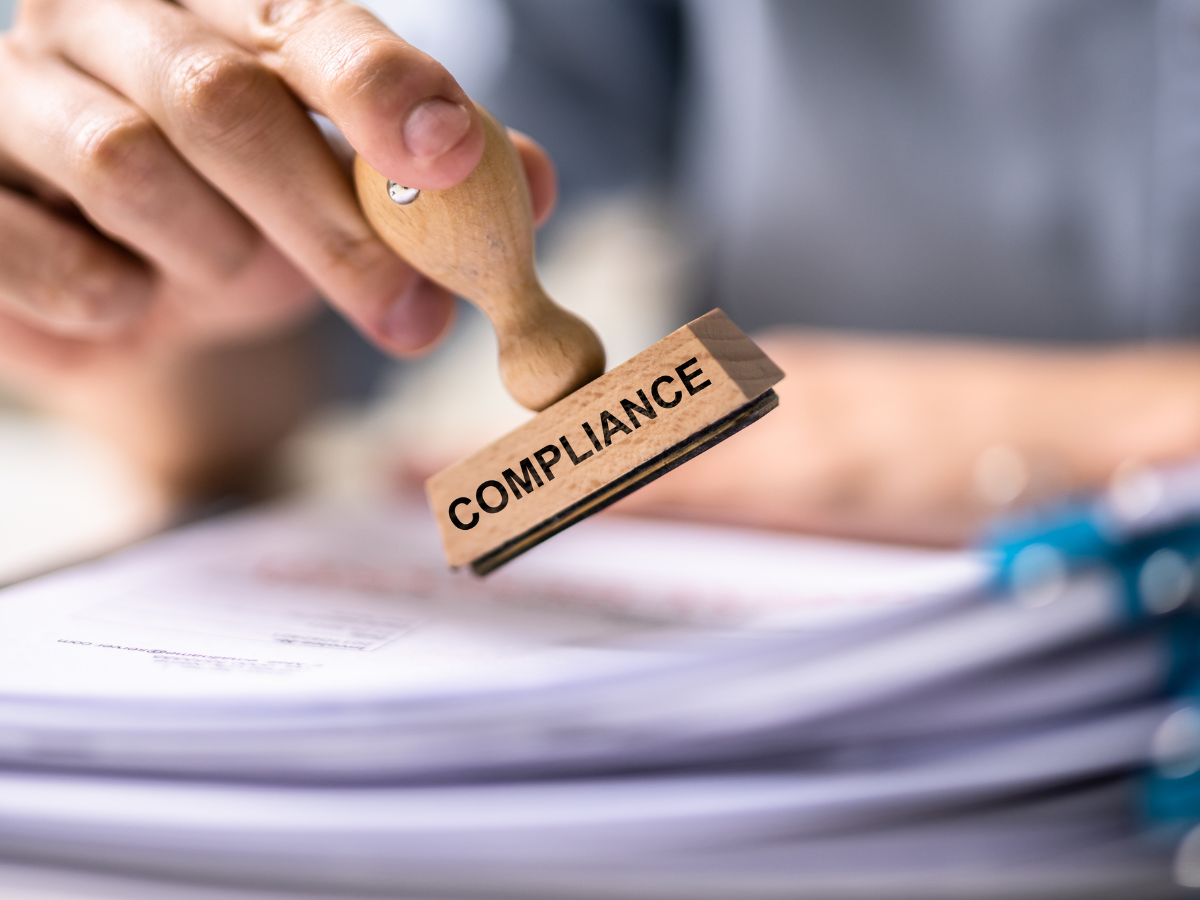 Person stamping a document labeled “Compliance,” representing eye care compliance in optometry and ophthalmology practices.