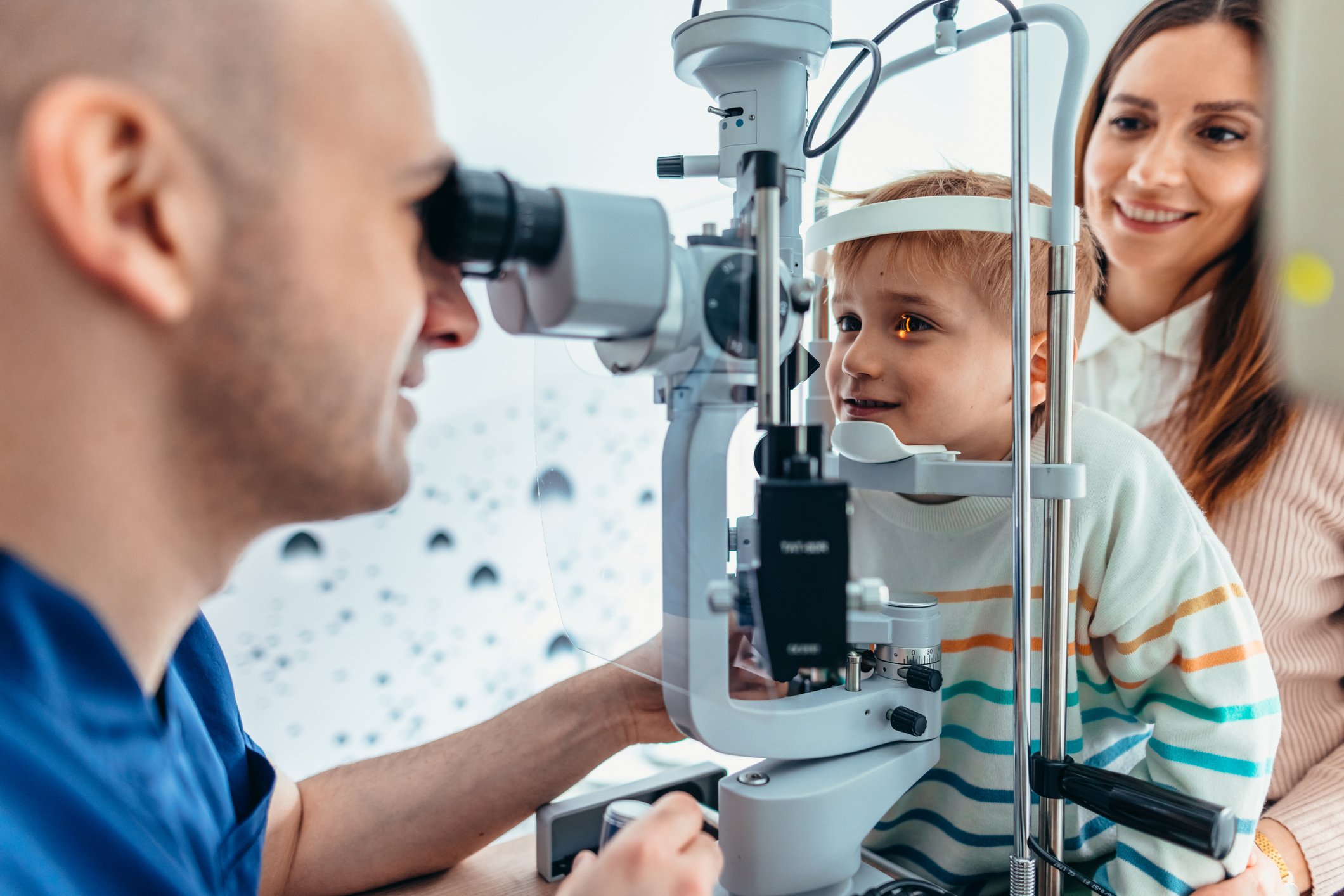 Optometrist examining a child’s eyes during a pediatric eye exam with parent present.