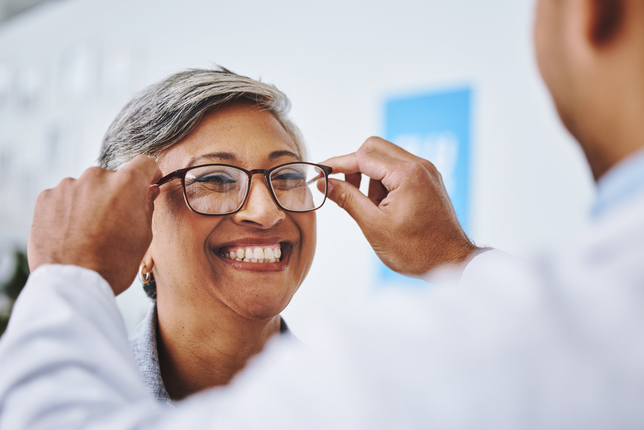Optician placing glasses on a smiling female patient