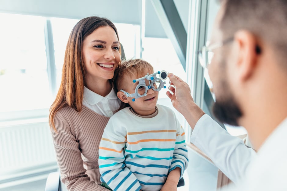 Woman holding her son and smiling during his eye exam, showing patient engagement in optometry.