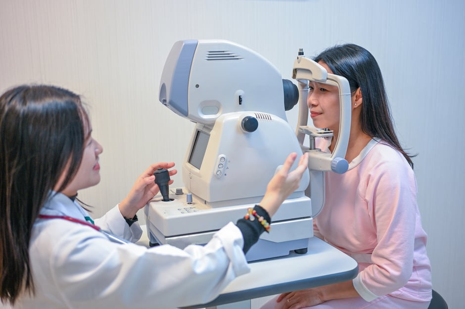 Ophthalmology staff operating diagnostic imaging equipment while performing an eye exam on a patient.