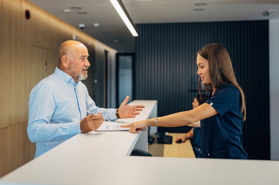 Male patient speaking with a front desk staff member in an ophthalmology clinic during the check-in process.