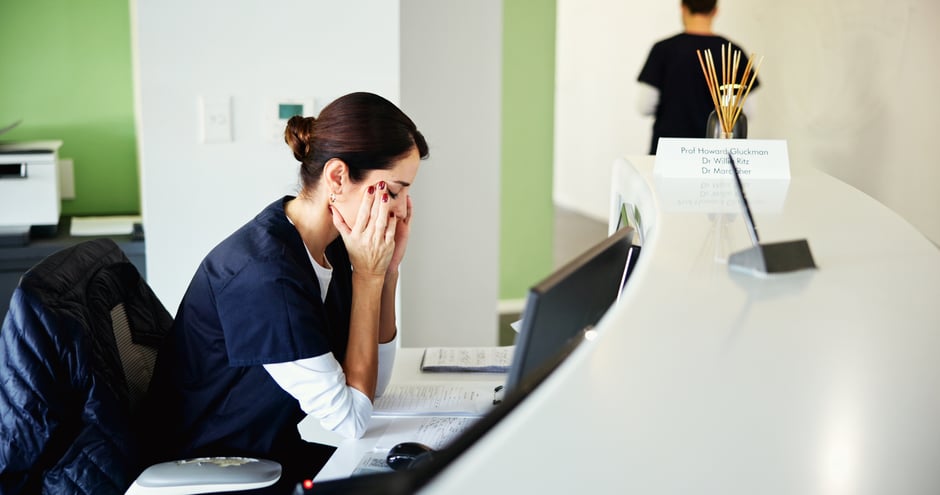 Front desk staff member appearing stressed while using an ophthalmology EHR at her computer.