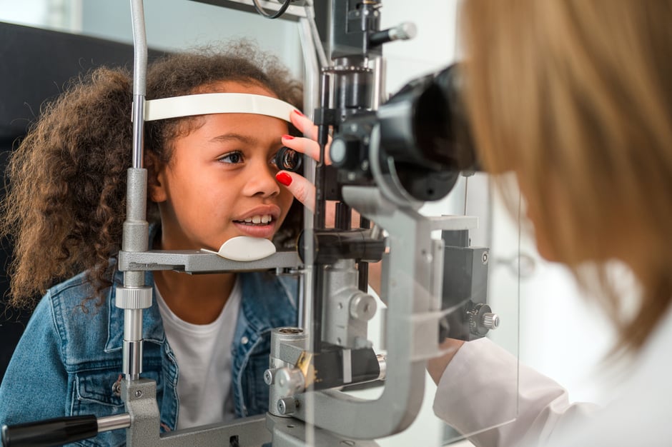 Optometrist performing a slit-lamp eye exam on a pediatric patient in an ophthalmology setting.