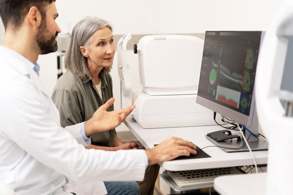 Ophthalmologist explaining diagnosis to senior patient using computer in clinic