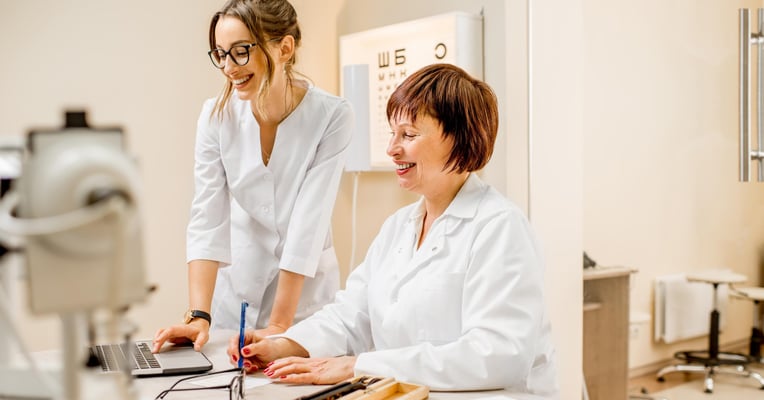 Senior woman ophthalmologist with young female assistant working with laptop at the office