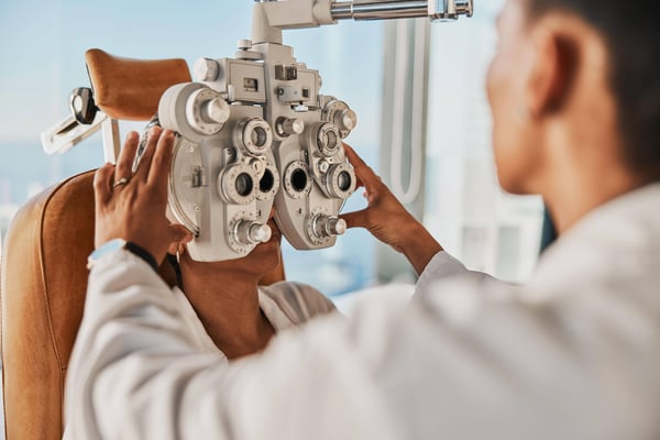 Senior optometry woman, eye exam patient and medical goal in hospital, consultation room and office with help. Elderly optician, eyesight test and phoropter for wellness, health and vision analysis